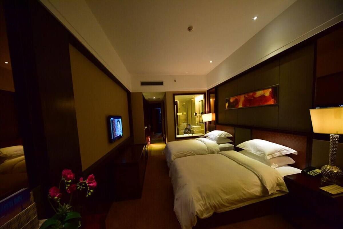 A hotel room with a large bed, bedside tables, a TV, and a bathroom visible through an open door.