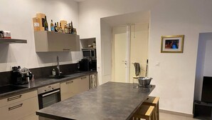 Een moderne keuken met een centraal eiland, ingebouwde apparatuur en een zithoek met houten krukken.