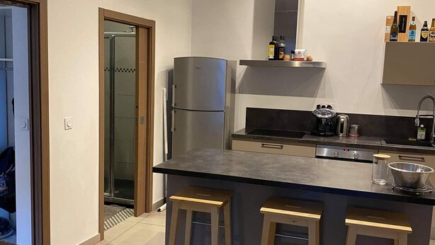 Een moderne keuken met een centraal eiland, twee krukken, een koelkast en een inbouwoven.