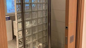 Een douche met glazen wanden, een zwart-wit betegelde vloer, een houten deur en uitzicht op een bakstenen muur door het glas.