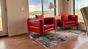 Uma sala de estar moderna com uma janela ampla, poltronas de couro vermelho, um tapete estampado e um abajur.