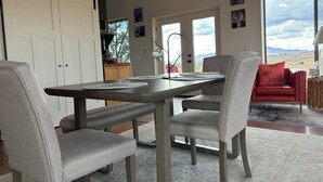 Uma sala de jantar com mesa, cadeiras e vista para o exterior.