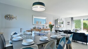A dining area with a table set for four, chairs, a pendant light, a fish-shaped shelf, a framed picture, and a view of greenery outside. - Les Daules (Cancale)