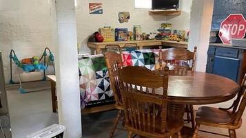 A dining area with a round wooden table and chairs, a baby swing, and a small white appliance.