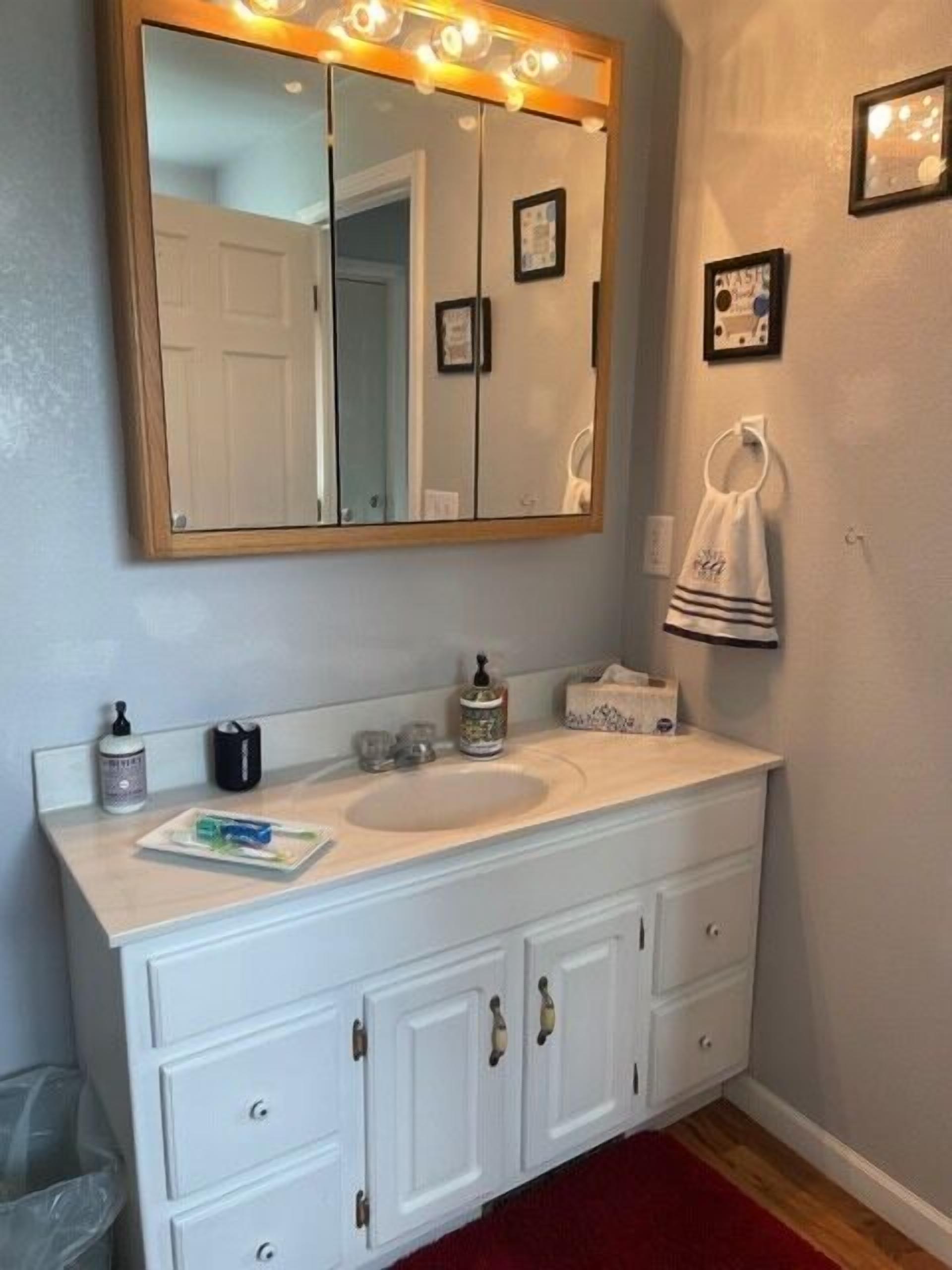 A bathroom with a large mirror, white vanity, and a red carpet.