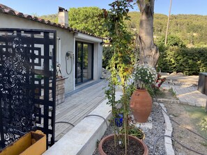 Une maison moderne avec un toit en tuiles, une porte en verre et un jardin agrémenté de plantes en pot et d’un arbre.