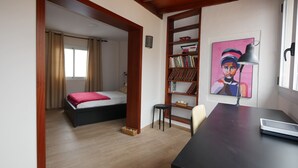 Une petite pièce comprenant un lit, un bureau, une bibliothèque et un tableau.