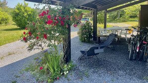 A covered outdoor seating area with a pergola, a gravel path, and a row of bicycles. - Soustons Grande Propriété Dans un Écrin de Verdure en Lisière de Forêt (Soustons)