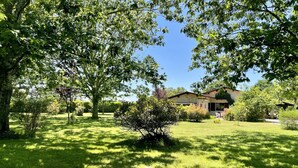 A well-maintained grassy area with mature trees and a building in the background. - Soustons Grande Propriété Dans un Écrin de Verdure en Lisière de Forêt (Soustons)