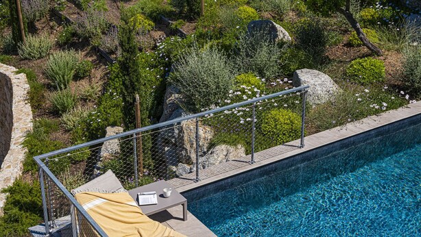En swimmingpool med solstolar och utsikt över en vackert anlagd trädgård.