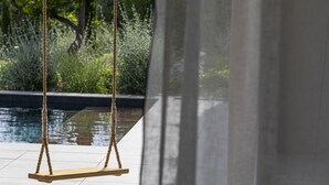 A wooden swing suspended by thick ropes over a tiled patio with a pool in the background. - Casa Baia Estate ★★★★★ (Calvi)