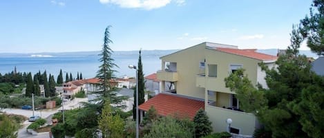 A coastal residential area with a modern two-story building, a paved driveway, and a view of the sea.