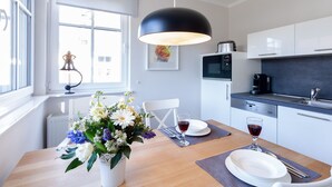 A modern kitchen with white cabinets, a black pendant light, and a dining table set with plates, glasses, and a vase of flowers. - Fewo am Horizont No3 Exklusivgenießen in Zingst (Zingst)