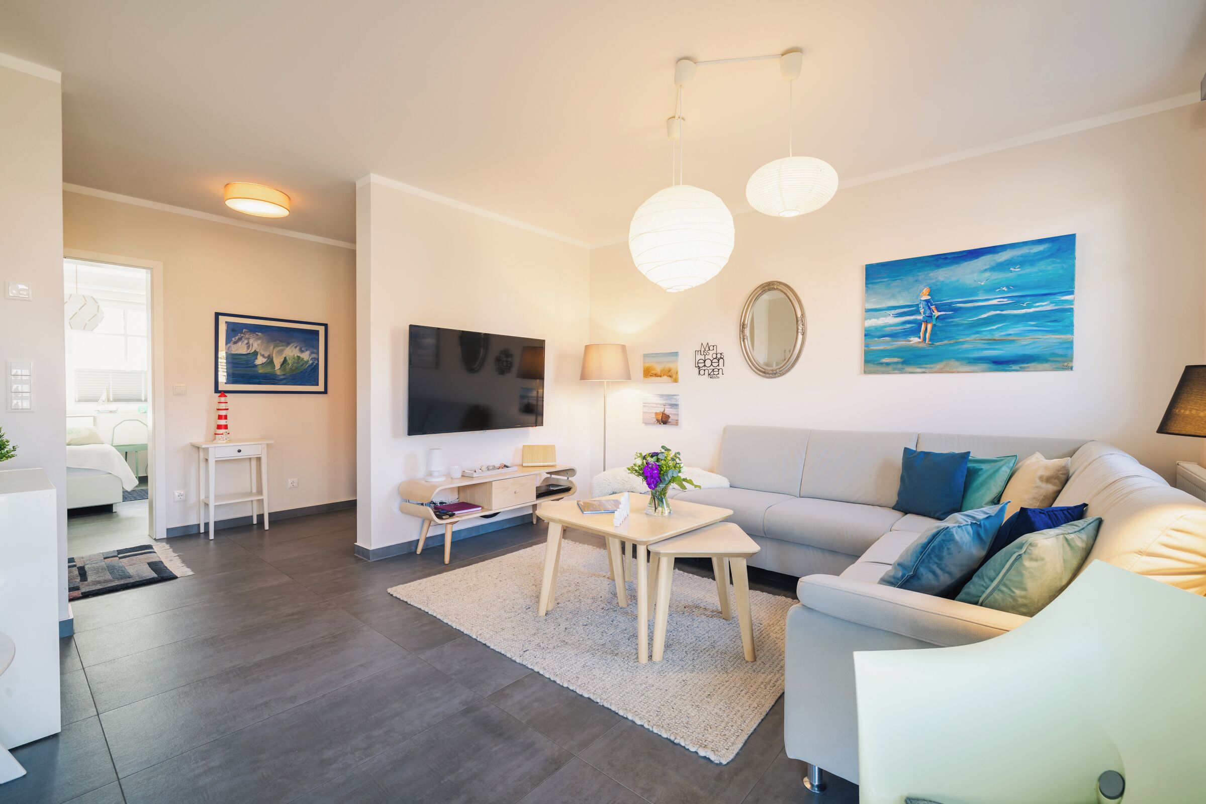 A modern living room with a sofa, coffee table, TV, and artwork on the walls.