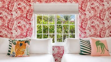 A room with two beds, a window with blinds, and a tropical leaf pattern on the walls.