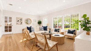 A spacious living room with a sofa, chairs, a coffee table, and large windows offering a view of greenery. - Brickell Oasis | Heated Pool, Fire Pit + Mini Golf (Miami)
