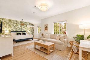 A modern living room with a sofa, a coffee table, a TV, and a large window. - Brickell Oasis | Heated Pool, Fire Pit + Mini Golf (Miami)