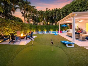 Un jardin bien entretenu avec un green d’entraînement au golf, des chaises longues et un espace piscine.