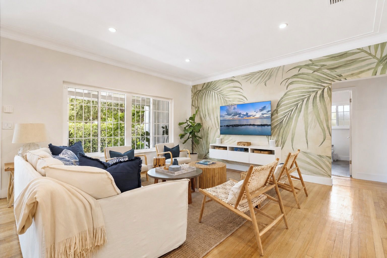 A spacious living room with a sofa, chairs, a coffee table, and a TV mounted on the wall.