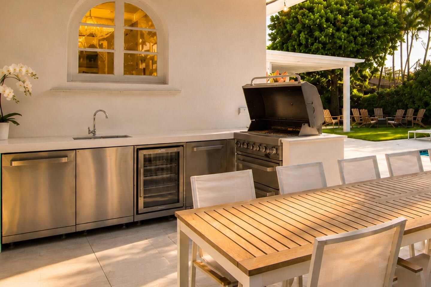 A modern outdoor kitchen with stainless steel appliances, a dining table, and chairs.