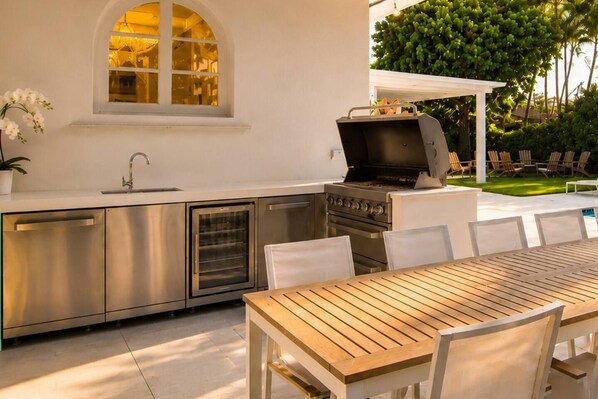 A modern outdoor kitchen with stainless steel appliances, a dining table, and chairs.