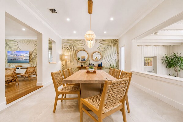 A dining area with a wooden table and wicker chairs, a large mirror, and a view of the outdoors.