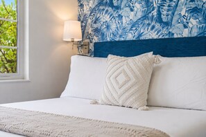 Un lit bien fait, avec une tête de lit à motifs blancs et bleus, un oreiller blanc et une lampe de chevet.
