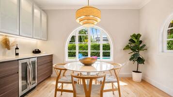 Uma cozinha moderna com uma mesa de jantar redonda, cadeiras de madeira, um lustre pendente e vista para uma piscina através de uma grande janela em arco.