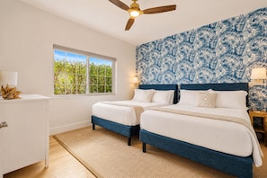 A bedroom with two beds, a window with a view of greenery, a ceiling fan, and a wall with a leaf pattern. - Brickell Oasis | Heated Pool, Fire Pit + Mini Golf (Miami)