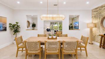 A dining area with a wooden table and woven chairs, a pendant light, and a view of the outdoors through a window.