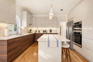 A modern kitchen with a central island, stainless steel appliances, and wooden cabinetry. - Saltwater Pool, Fire Pit | Gated Brickell Oasis (Miami)