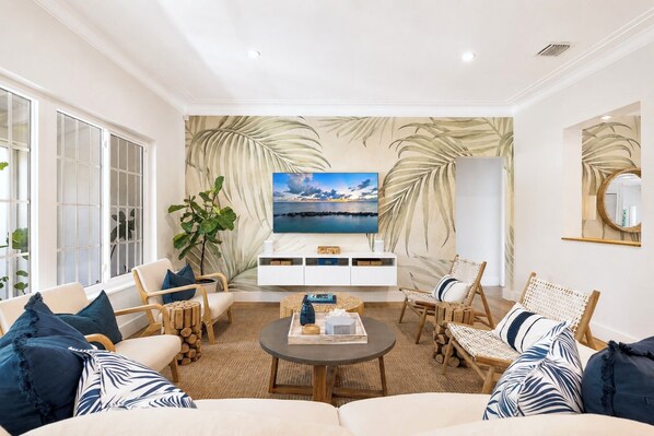 A living room with a large flat-screen TV, a white entertainment unit, and a large plant.