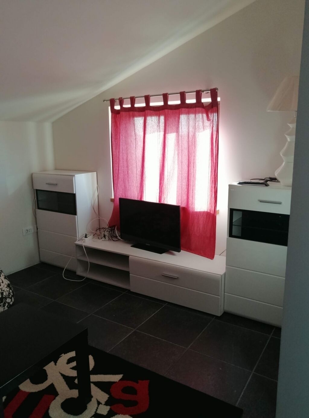 Un espace de vie compact comprenant un téléviseur posé sur un meuble, une petite armoire blanche et un rideau rouge.