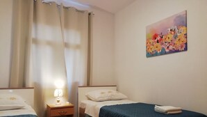Et hotelværelse med to senge, et natbord med en lampe, et blomsterbillede på væggen og et trægulv.