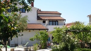 A two-story house with a tiled roof, a garden with grass and plants, and a clear blue sky. - Apartment in Funtana with Terrace, Air condition, WIFI, Washing machine (4982-7) (Funtana)