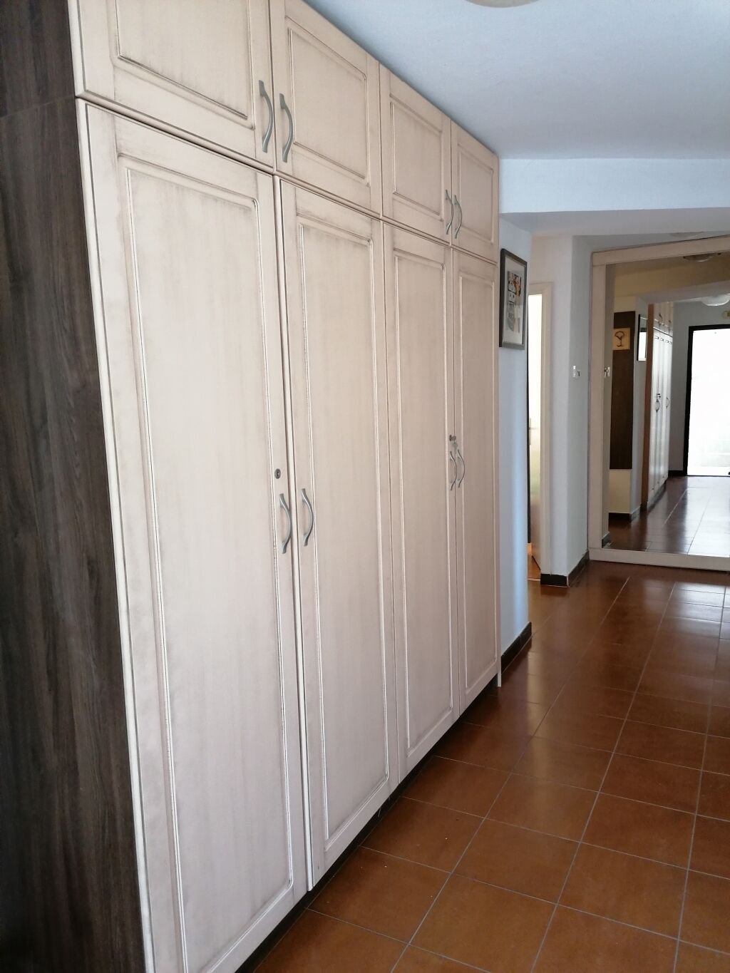 A spacious hallway with a large white wardrobe and a wooden floor.