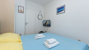 Quarto de hotel com cama, televisão, porta e parede com duas imagens.