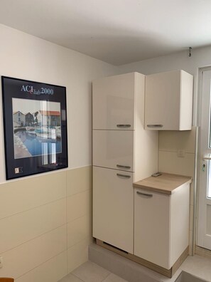 Functional kitchen area with cabinet and workspace, featuring a framed coastal scene.