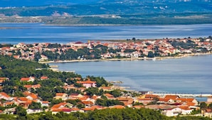 A coastal town with red-roofed houses, a marina, and a hilly backdrop.