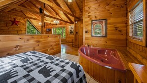 A wooden cabin with a large bed, a red bathtub, and a ceiling fan. - Dog Friendly, Mtn Views, Wood Fireplaces, Hot Tub, Pool Table, Pools, Pickleball (Gatlinburg)