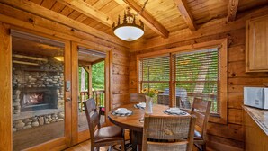 A wooden cabin interior with a stone fireplace, wooden dining table, and chairs. - Dog Friendly, Mtn Views, Wood Fireplaces, Hot Tub, Pool Table, Pools, Pickleball (Gatlinburg)