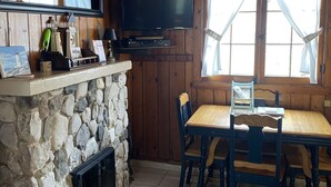 A cozy cabin interior with a stone fireplace, wooden walls, a dining table with chairs, and a mounted television. - Parkview Cottage #7 - 1/2 block to city beach (Ludington)