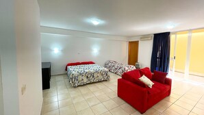 Amplia sala de estar con dos camas, un sofá rojo y una pequeña mesa.