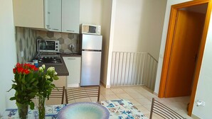 Cocina compacta con microondas, estufa y refrigerador. Hay una mesa de comedor con un plato decorativo y un florero.