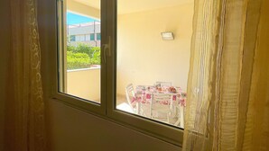 Una habitación con ventana, una mesa con sillas y vistas a un edificio y vegetación.