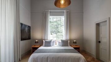 A bedroom with a large bed, a window with curtains, a painting on the wall, and a door.
