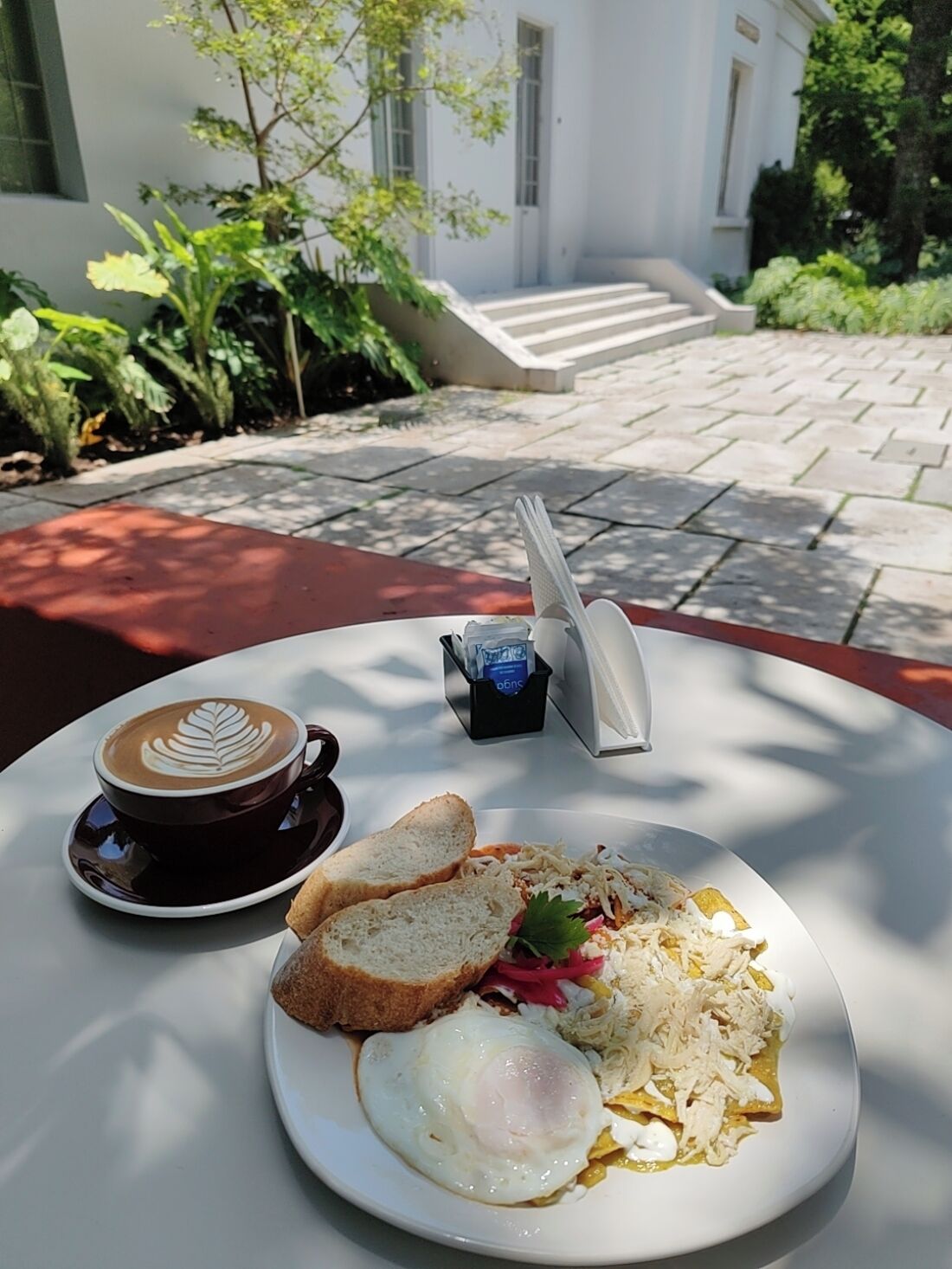 Ein Frühstückstisch im Freien mit Kaffee, Toast und einem Teller mit Eiern und zerrupftem Hähnchen.