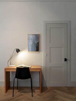 Un espacio de trabajo con escritorio, silla, lámpara y un cuadro en la pared.
