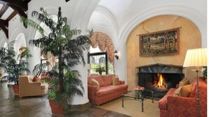 Un vestíbulo amplio con chimenea, sofás rojos y plantas en macetas.
