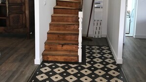 A staircase with wooden steps leading to a landing, a patterned rug on the floor, and a white wall with a door on the right. - Maison à 100m de la Plage (Treffiagat)